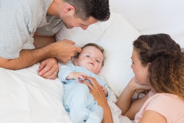 Loving parents playing with baby in bed